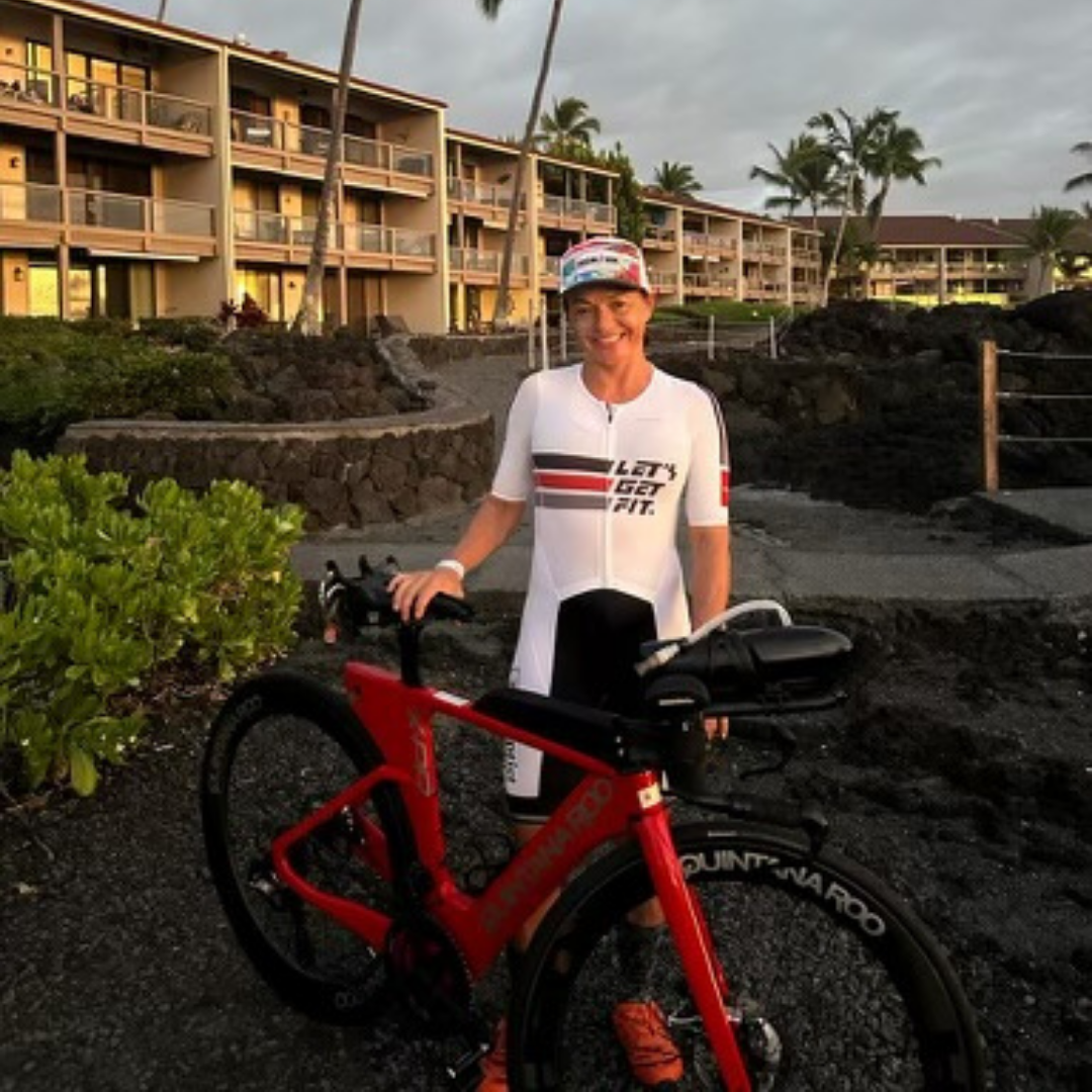 Let's Get Fit team member in a custom white Pavé trisuit beside a triathlon bike